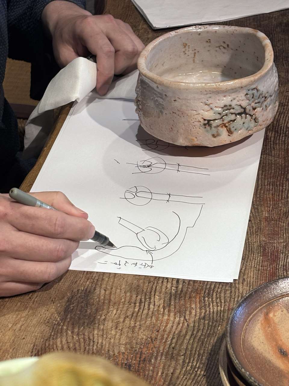Un cuenco de cerámica sobre una mesa junto a notas y dibujos de taller.
