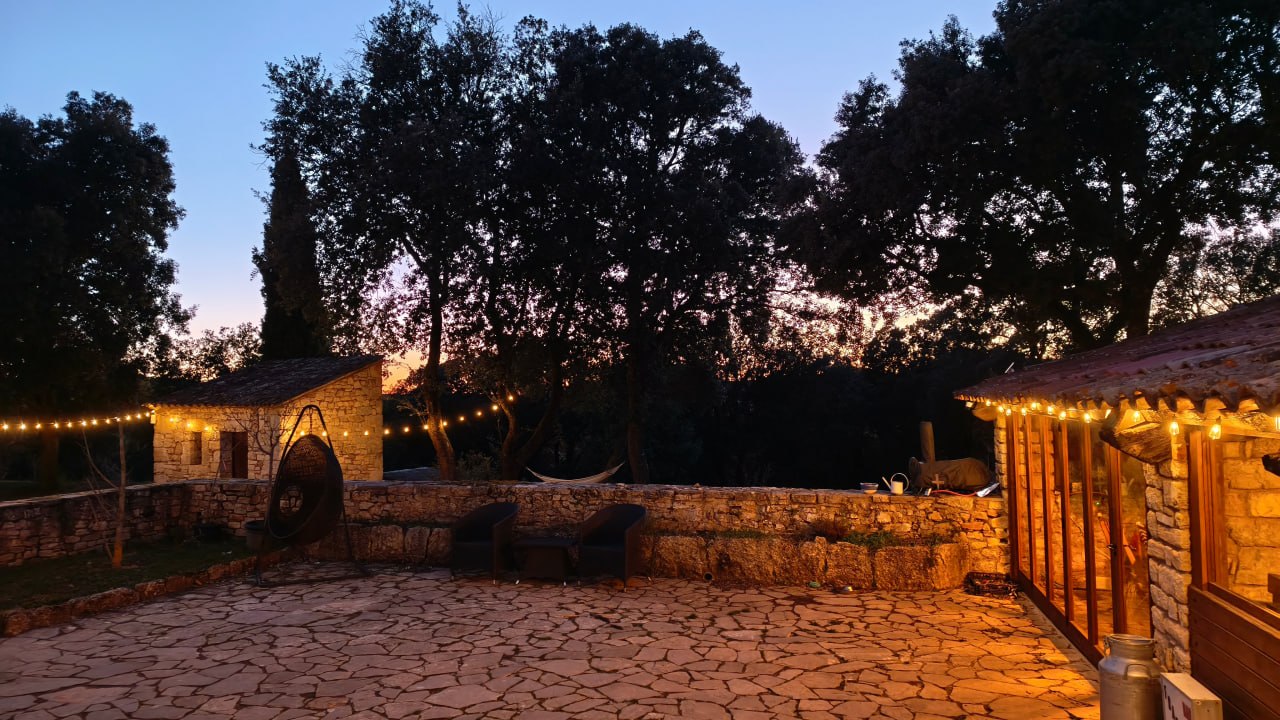 The stone terrace at Can Brull at dusk, with warm lights and the forest behind it.