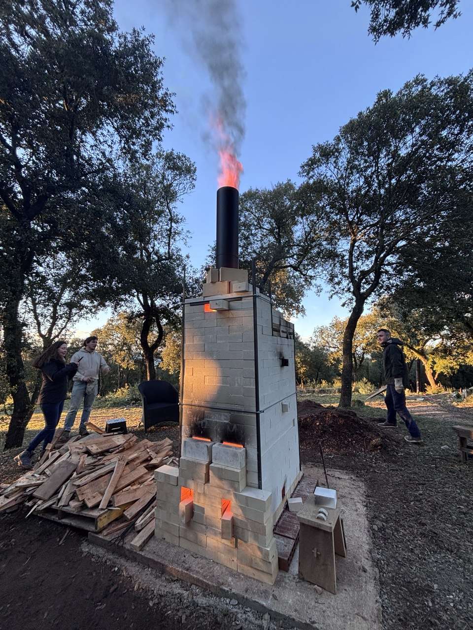 Un pequeño horno de leña encendido al aire libre en Can Brull, con llama y humo saliendo por la chimenea.