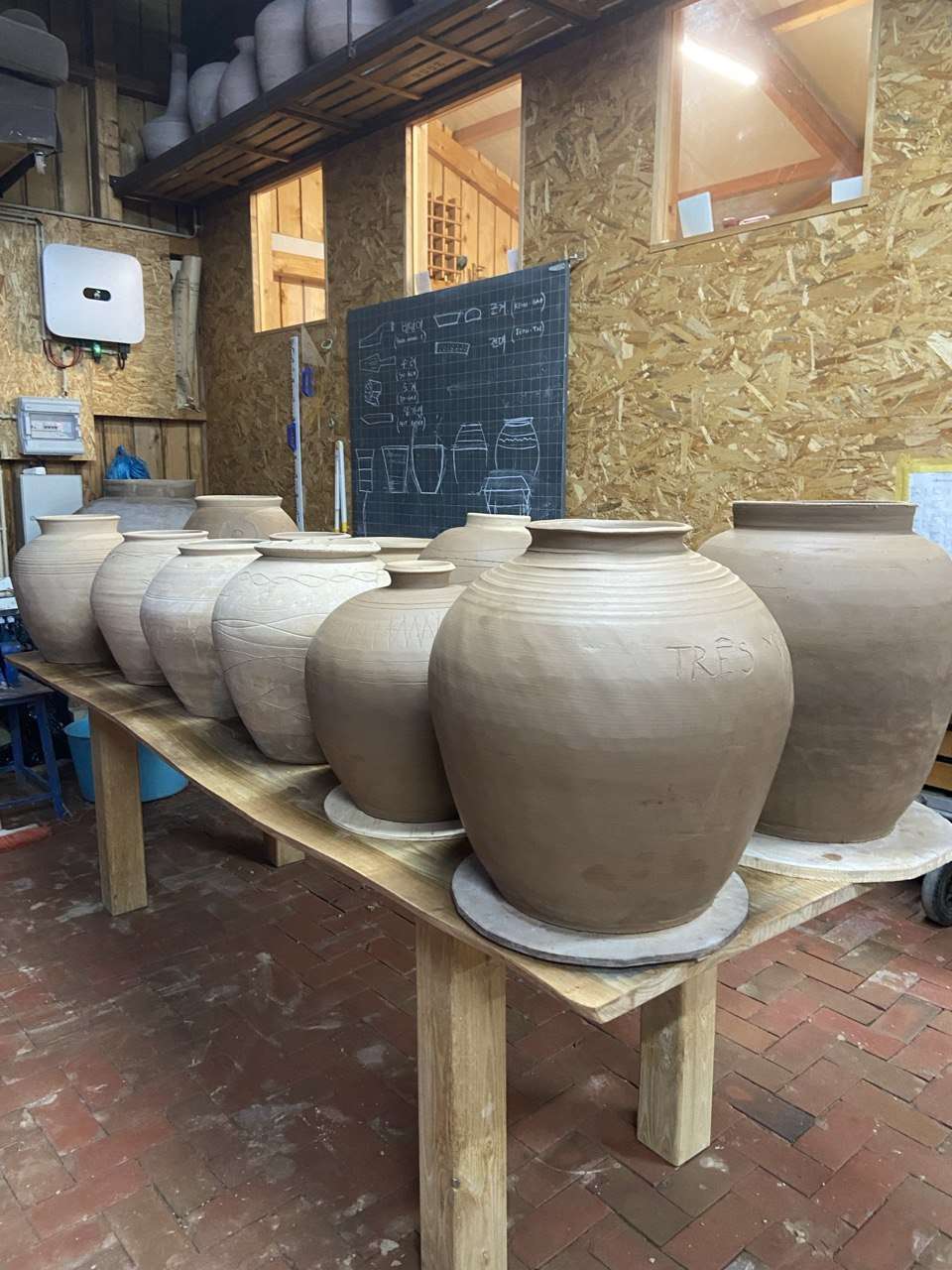 Grandes vasijas de barro secándose sobre una mesa en el taller de cerámica.