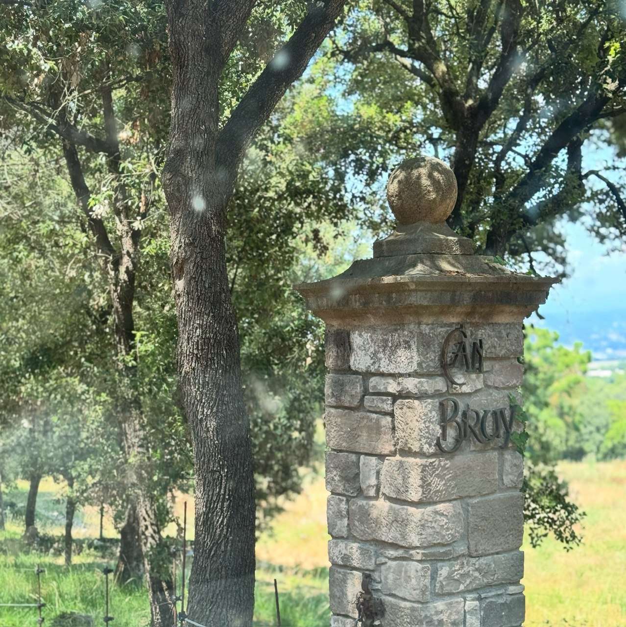 The stone entrance of the Can Brull masia, with visitors and dogs walking in.